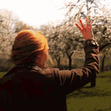 a woman with red hair is waving her hand in front of trees