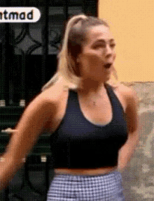 a woman in a black tank top and plaid shorts is standing in front of a building with the word mad on it