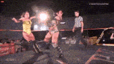 two women are wrestling in a ring while a referee stands nearby .