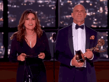 a man in a tuxedo and a woman in a black dress holding a trophy
