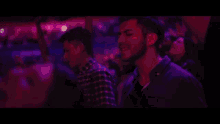 a man in a plaid shirt stands in a crowd of people at a party