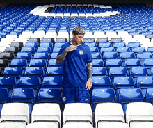 a man in a blue shirt is standing in a stadium with rows of blue and white seats