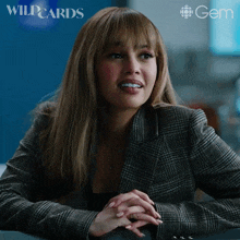 a woman in a plaid jacket sits at a table with her hands folded in front of a gem logo