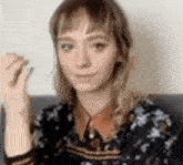 a woman in a floral shirt is sitting on a couch and making a face .