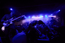 a man playing a guitar in front of a crowd with purple lights