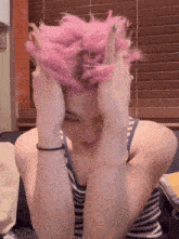 a person with pink hair is holding their head with their hands