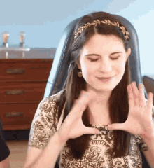 a woman wearing a headband with leaves on it is making a heart shape with her hands