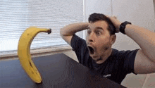 a man is sitting at a table with his hands on his head and a banana on the table .