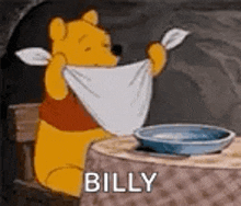 winnie the pooh is sitting at a table holding a towel around his neck and saying `` billy '' .