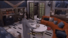 a man is standing in a living room with a couch and a table and says what the fuck .