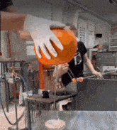 a man wearing gloves is holding a large orange ball in a glass studio .