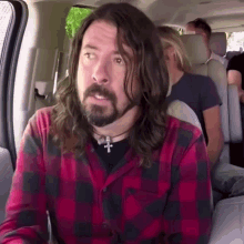 a man with long hair and a beard is sitting in the back seat of a car