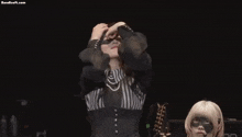 a woman is standing on a stage with her arms outstretched and a mask on her face .