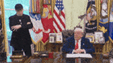 a man in a suit and tie is standing next to a man in a suit and tie sitting at a table .