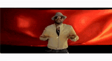 a man with a hat and sunglasses is dancing in front of a red background