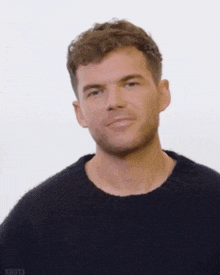 a man with a beard wearing a black sweater is waving his hand in front of a white background .