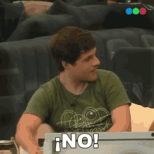a man in a green shirt is sitting in front of a laptop and says no