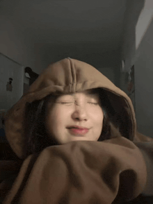 a woman wearing a brown hoodie with her eyes closed is laying on a bed .