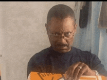 a man wearing glasses and a ring is holding a box that says ' eee ' on it