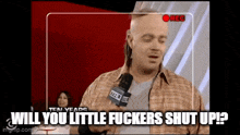 a man in a plaid shirt is holding a microphone and says " will you little fuckers shut up ? "