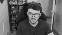 a man with glasses and a beard is sitting in a chair .