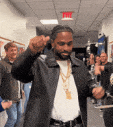 a man in a black jacket is dancing in a hallway with a red exit sign above him