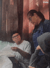 a man with glasses looks at a piece of paper while a woman stands behind him