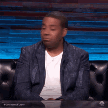 a man in a suit is sitting on a couch with the hashtag bringthefunny