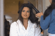 a woman in a white robe getting her hair blow dried