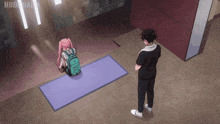 a girl with a backpack sits on a yoga mat while a man stands nearby