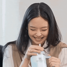 a woman with long black hair is smiling while holding a blue bottle