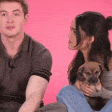 a man and a woman are sitting next to each other holding a small dog