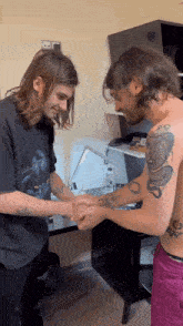 a man with a snake tattoo on his arm shakes hands with another shirtless man
