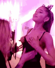 ariana grande is wearing a cat ear headband and taking off her bra while standing next to a woman .