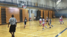 a group of kids are playing basketball in a gym with a referee watching