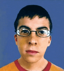 a young man wearing glasses and a red shirt looks at the camera .