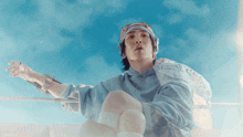 a man wearing a bandana and a blue hoodie looks up at the sky