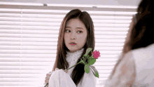 a woman is holding a red rose in her hand and looking at herself in the mirror .