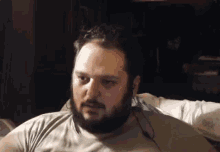 a man with a beard is sitting on a couch wearing headphones and looking at the camera .