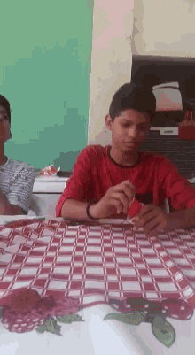 a boy in a red shirt is sitting at a table with a checkered table cloth