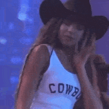 a woman wearing a cowboy hat and a white tank top is dancing .