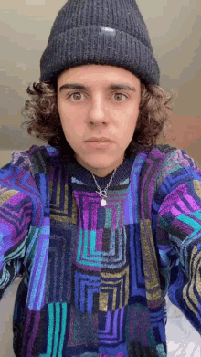 a young man with curly hair is wearing a beanie and a colorful sweater .
