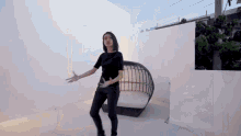 a woman in a black shirt and black pants is dancing in front of a white wall and a couch .