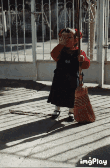 a little girl holding a broom in front of a fence