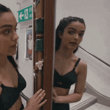 a woman looks at her reflection in a mirror with a green exit sign above her