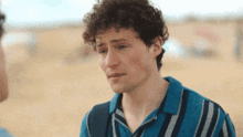 a young man with curly hair is wearing a blue striped shirt and talking to another man .