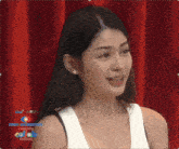 a woman in a white tank top is smiling in front of a red curtain with the words jenny big brother on it