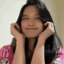a woman in a pink shirt is smiling with her eyes closed