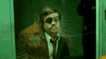 a man in a suit and tie with an eye patch is looking out of a window .