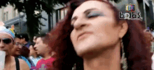 a woman with red hair and blue eyeshadow stands in front of a crowd of people with the word bolas in the corner